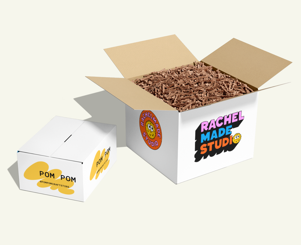 Two large white custom cardboard packages filled with corrugated packing paper and colorful “Rachel Made Studio” text and logo circular logo on the sides