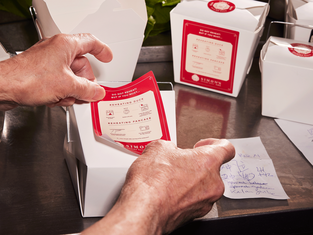 A red branded sticker being attached to a white cardboard box