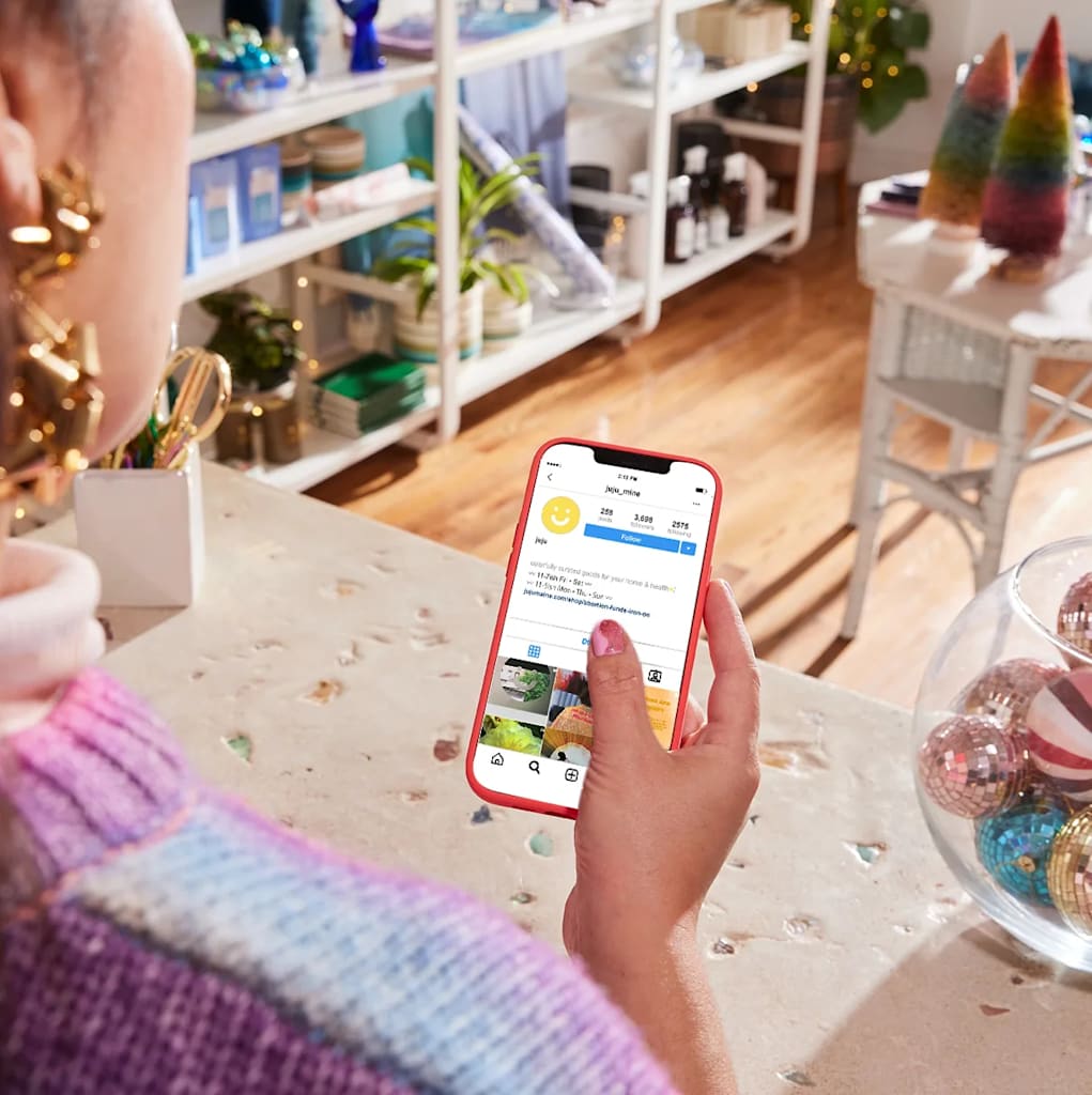 A woman surrounded by holiday decorum holding a phone with an Instagram account open