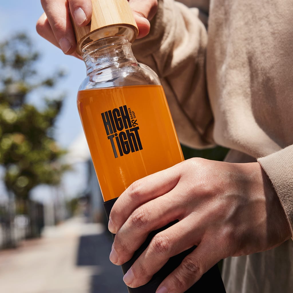 Hands uncapping a bambook lid from a stylish, custom glass water bottle branded with in bold, blocky font-based logo