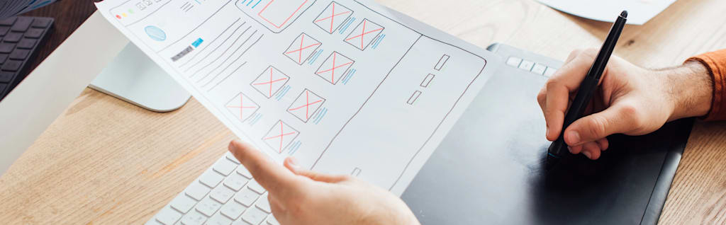 Hand sketches wireframes on table while looking at printed copy