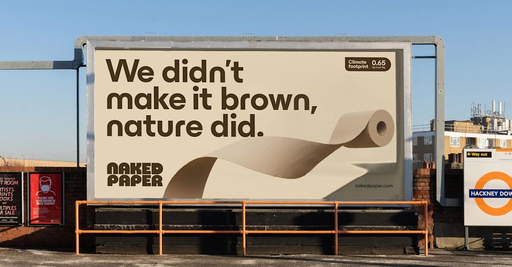 A billboard with a brown-toned advert for Naked Paper featuring an illustration of an unraveling toilet roll