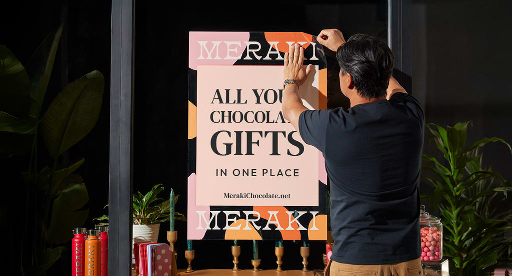 Homme accrochant une affiche typographique pour une marque de chocolat sur une vitrine
