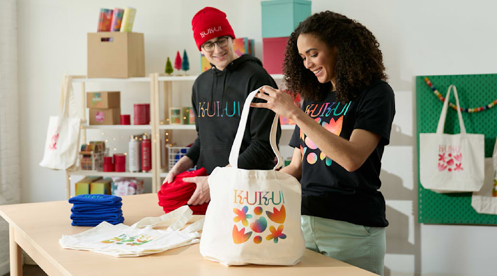 Two people organizing branded tote bags and beanies