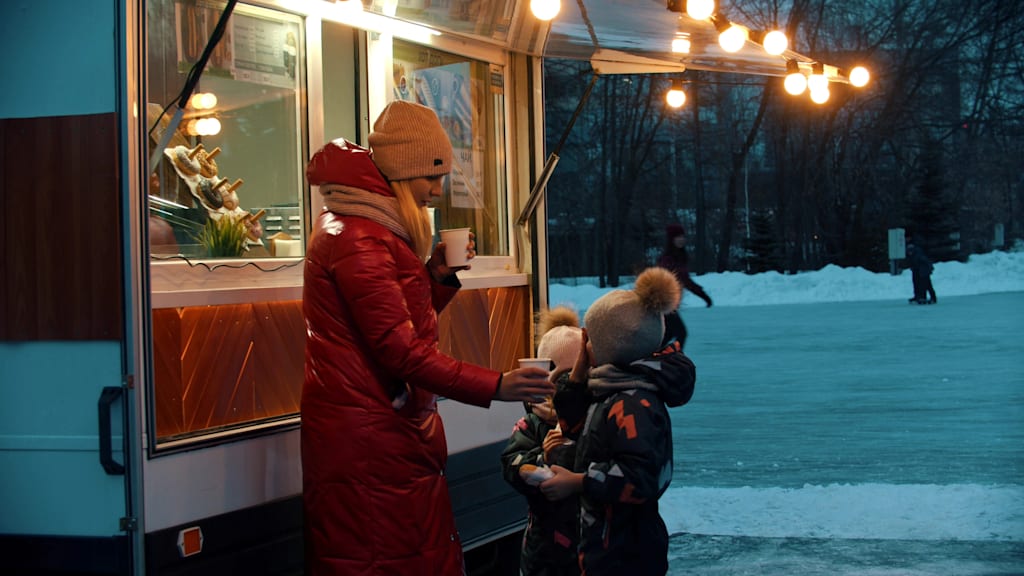 A family shares a hot beverage at a stand in the snow
