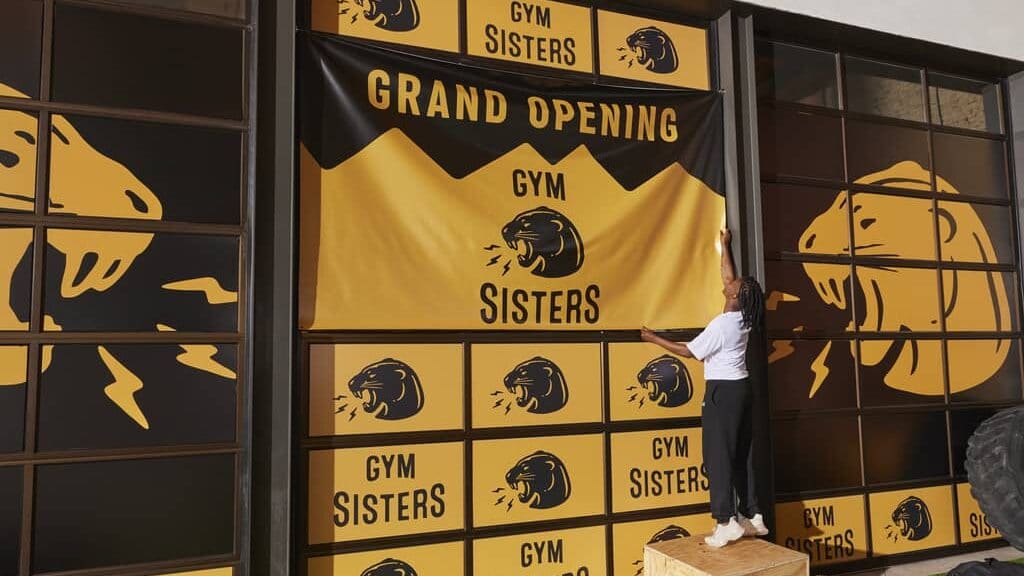 small business owner hanging a branded yellow banner in gym for a grand opening