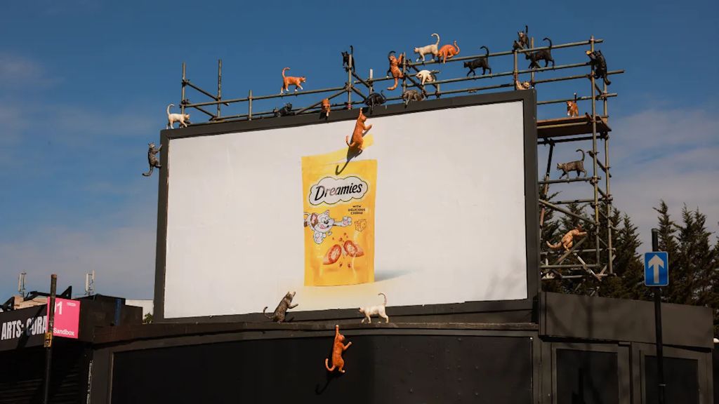 A photo of a DREAMIES OOH billboard surrounded by giant fiberglass cats of all colors—an example of the Mischief Marketing top marketing trend 2026