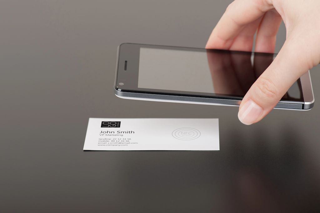A business card with a NFC symbol is being hovered over by a phone screen, viewed from the side