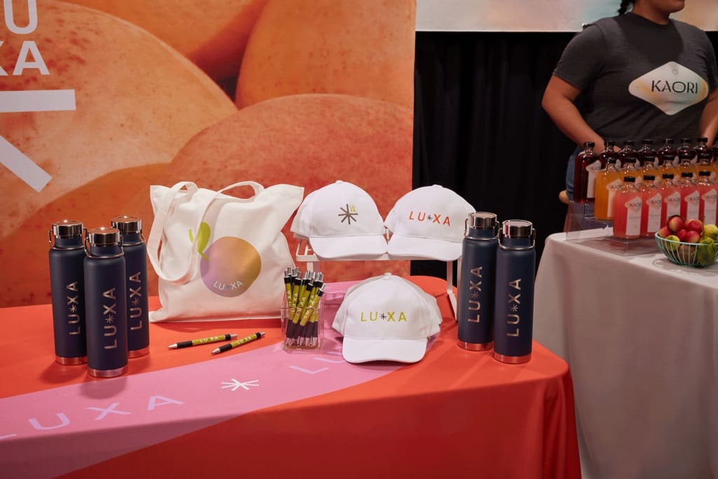 Trade show table displaying branded merch including caps, flasks and totes