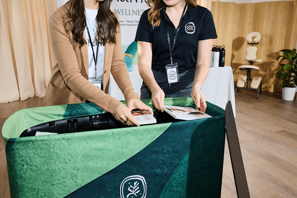 Two small business owners at Ananya wellness stand reviewing leaflets at a trade show table with a green velvet tablecloth.