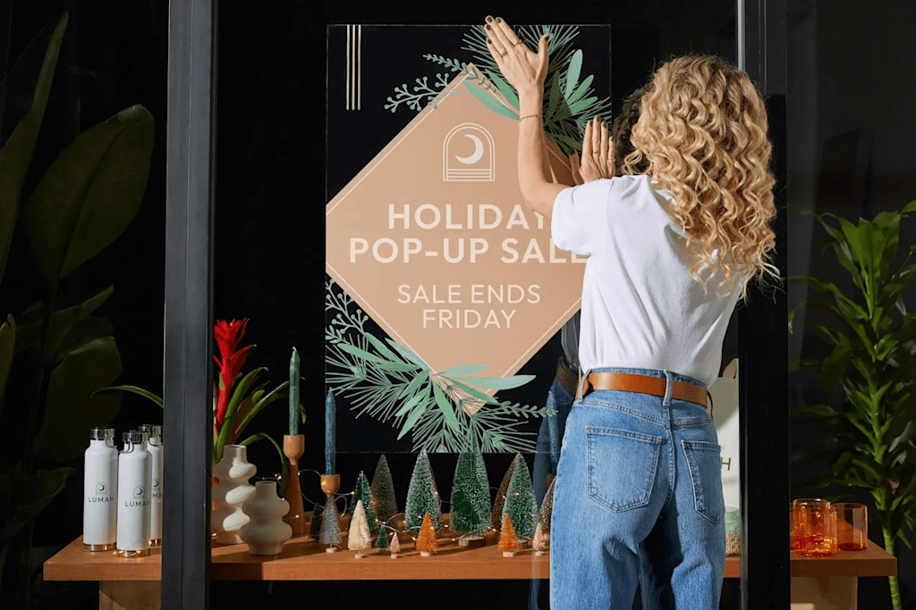 Une commerçante qui installe un panneau de Noël en vitrine