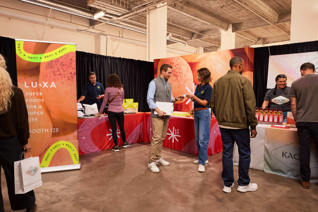 People interacting at branded booths during a trade show, showcasing event marketing materials like banners, table covers and promotional displays
