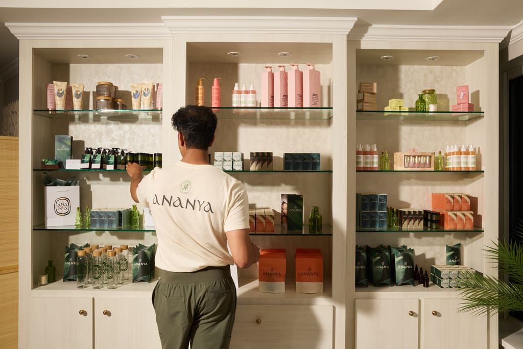 Employee wearing a branded T-shirt arranging products on shelves in a spa retail space