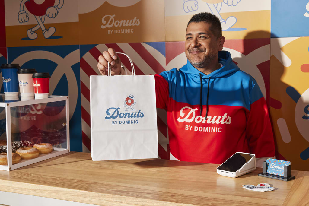 Man in doughnut shop wearing branded merch handing over a branded bag
