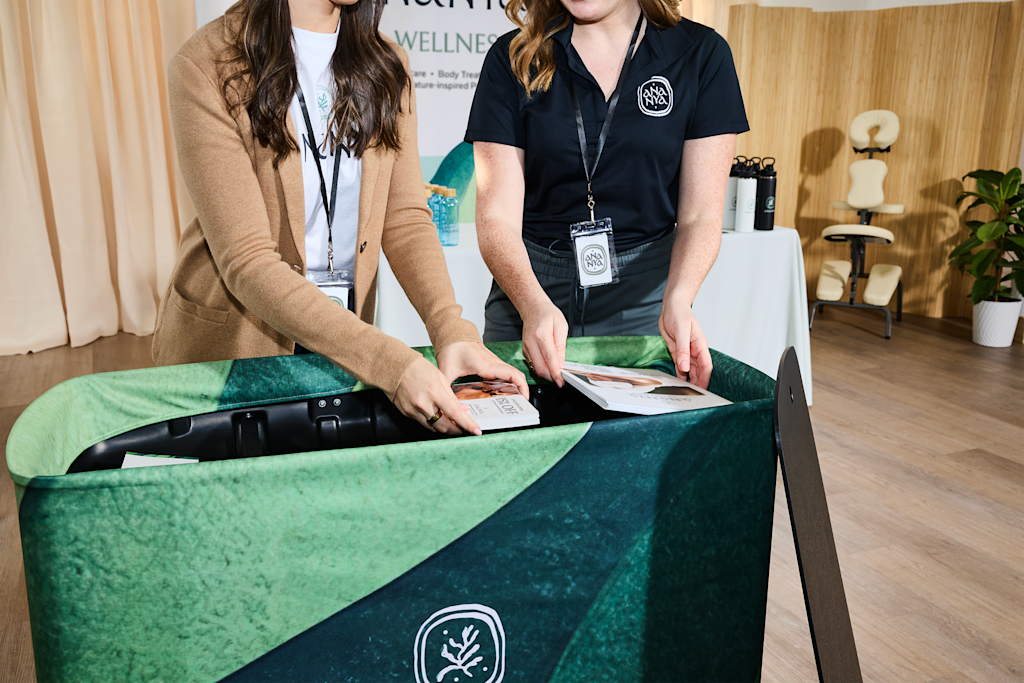 Two small business owners at Ananya wellness stand reviewing leaflets at a trade show table with a green velvet tablecloth.