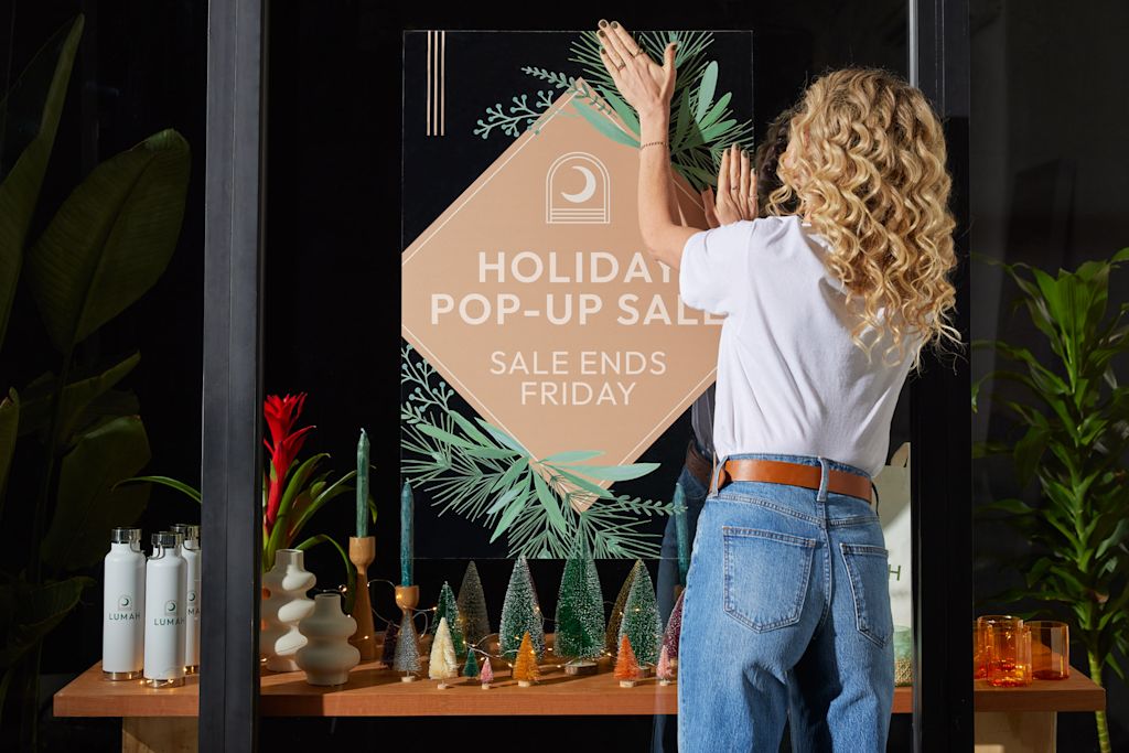 A person hanging up a sign with holiday decoration