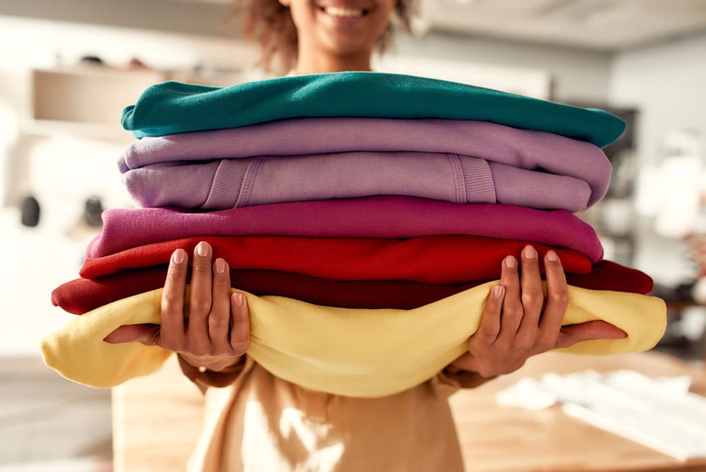 Woman holding stack of hoodies and showing off hoodie fabrics.