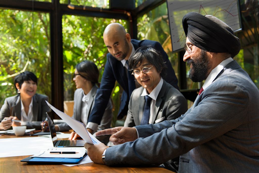 Business team reviewing documents together in a meeting room, with charts visible on screens in the background.