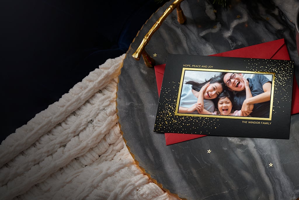 A physical Christmas card with a family photo and gold foil accents