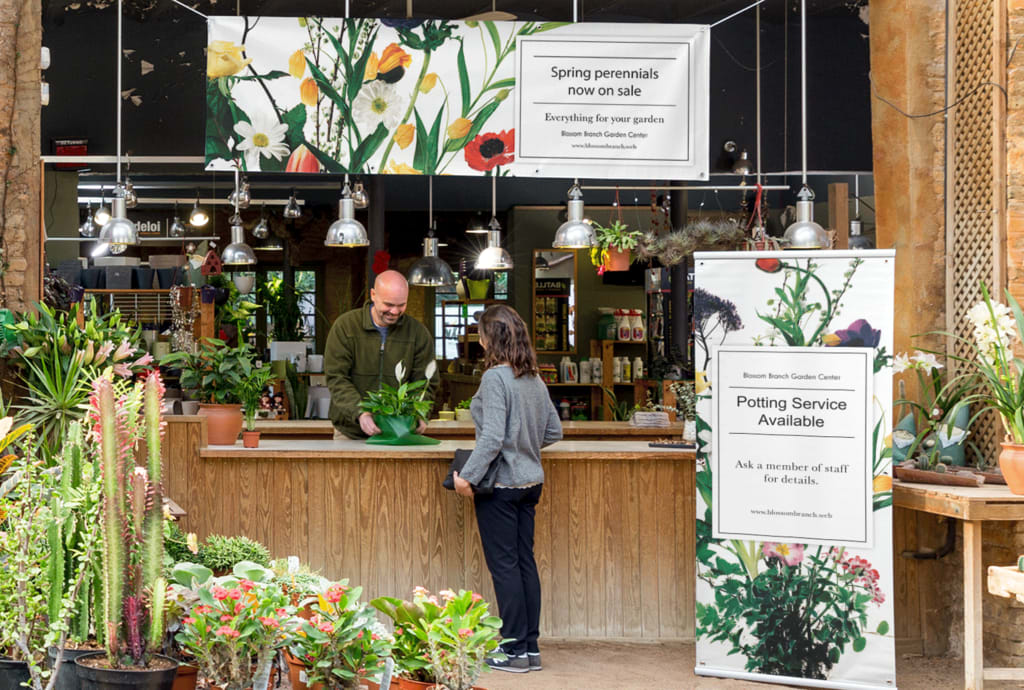 Customer being served in a plant shop with a retractable banner by the desk offering potting services