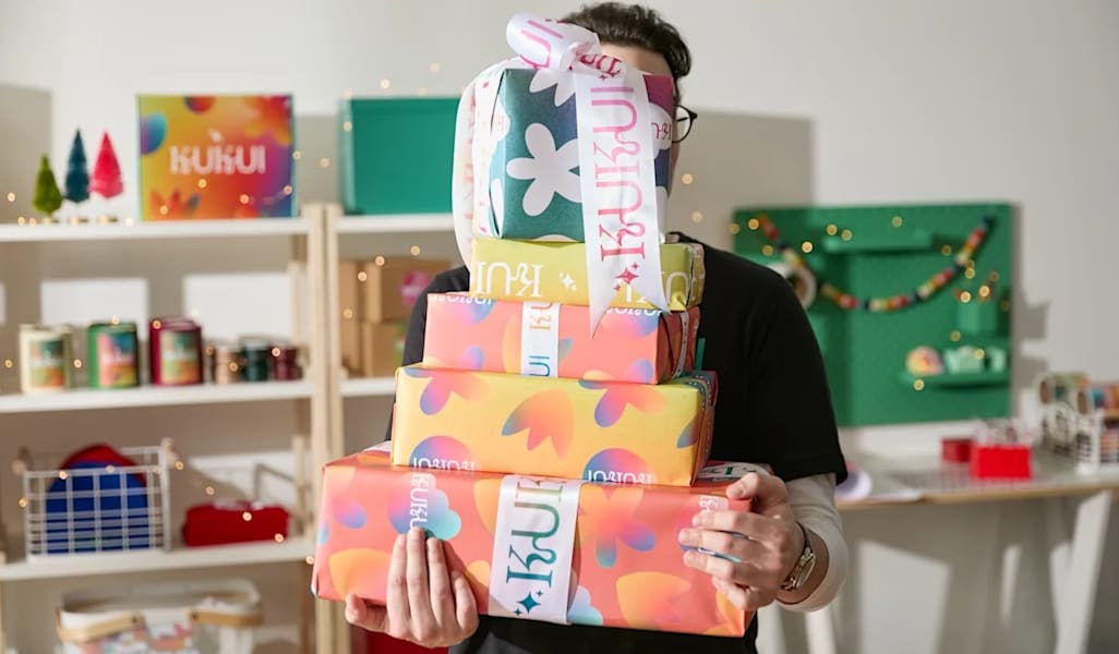 Homme portant une pile de cadeaux colorés dans ses bras, tellement nombreux qu'ils couvrent son visa