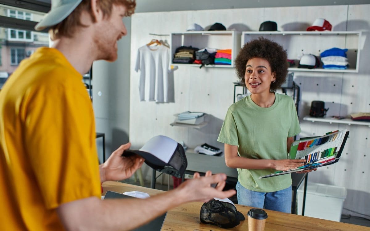Two people smiling as they look at fabric samples and a laptop in a print studio
