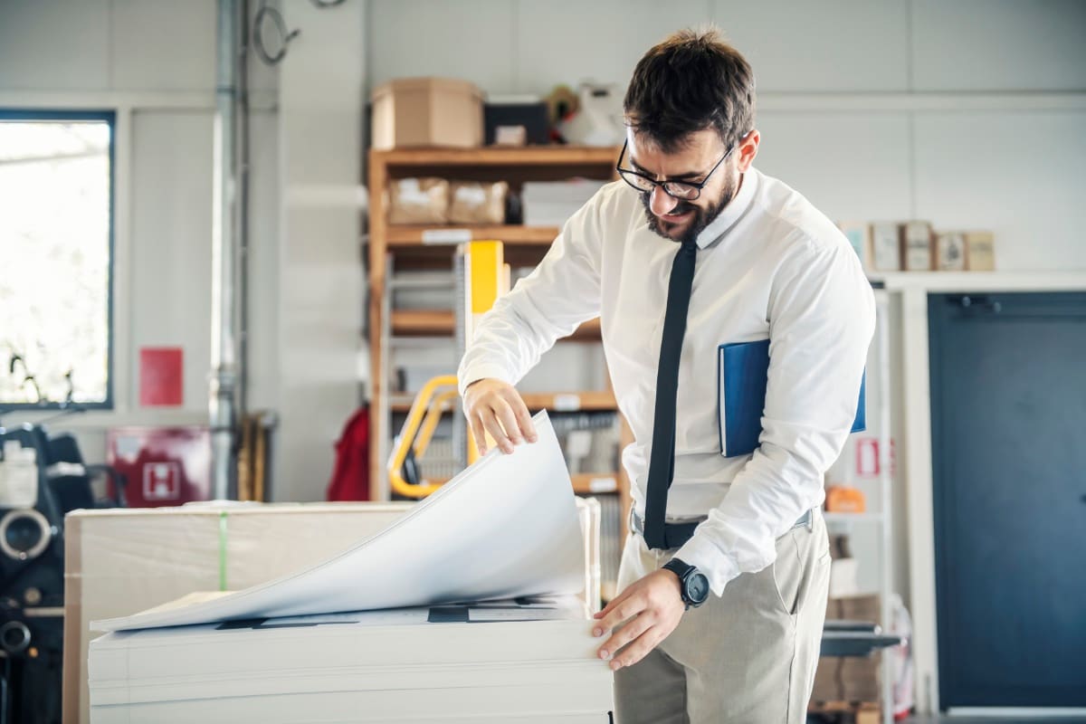 A man in a printing shop holding a large stack of paper