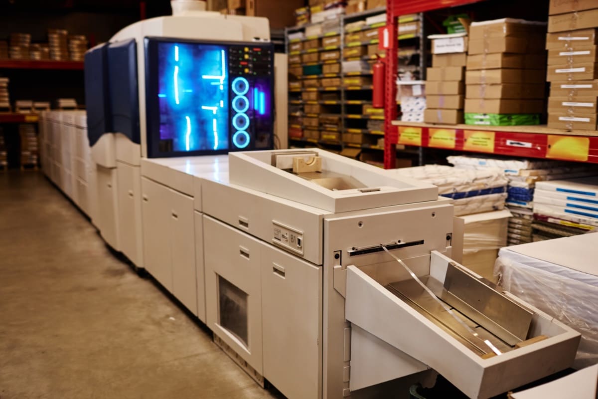 A printing workshop with a printing machine glowing blue at the center of the frame
