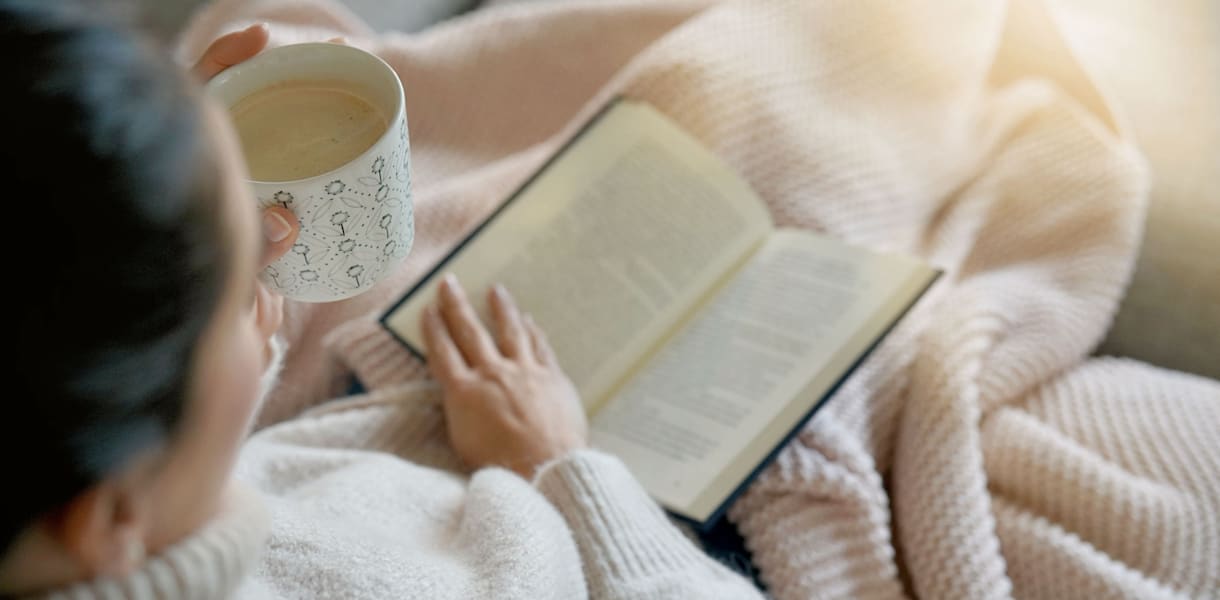 Cosy brunette at home on couch with hot drink and reading
