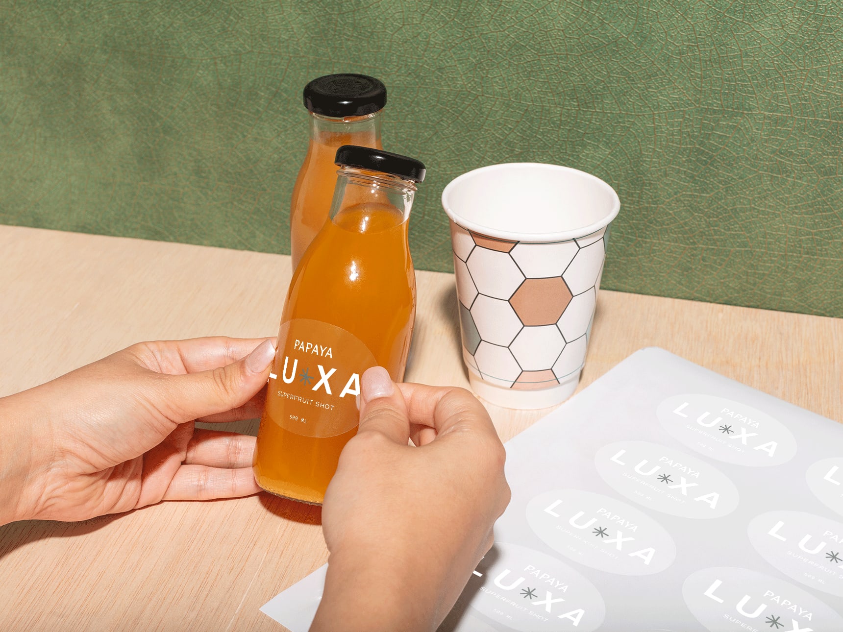 A person applying a branded clear sticker from a sticker sheet on a bottle as a label