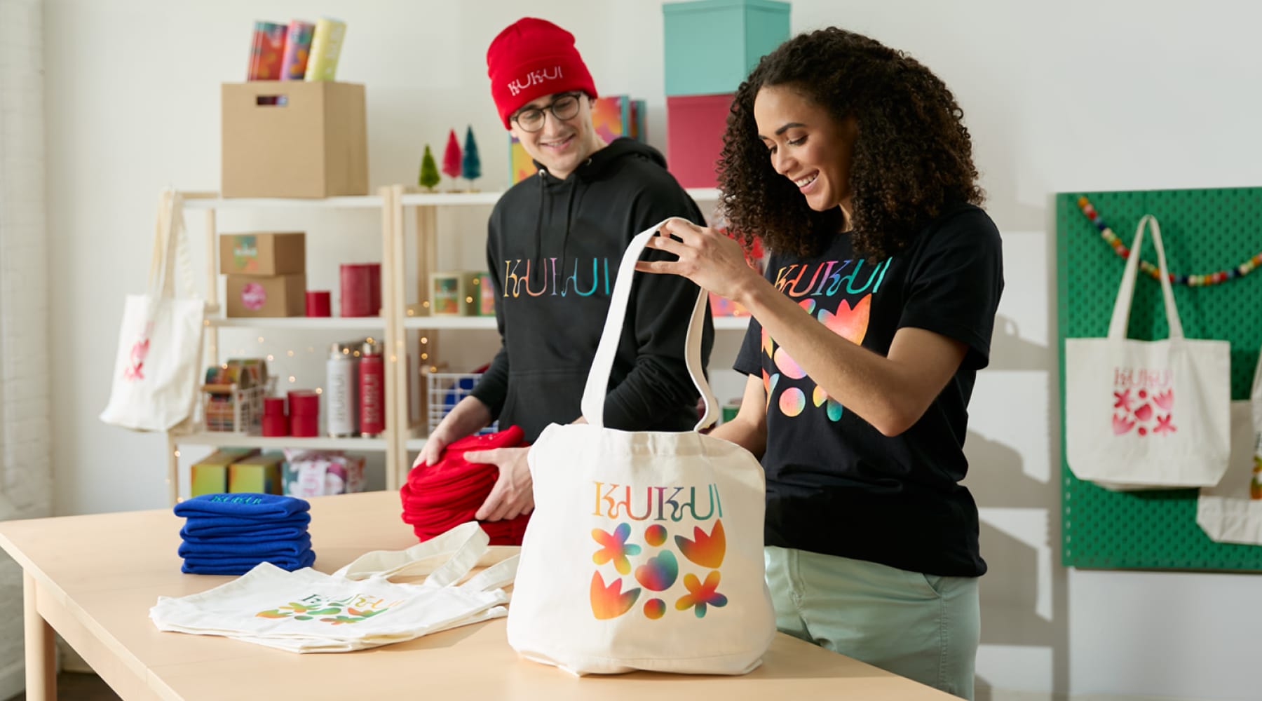 Two people organizing branded tote bags and beanies