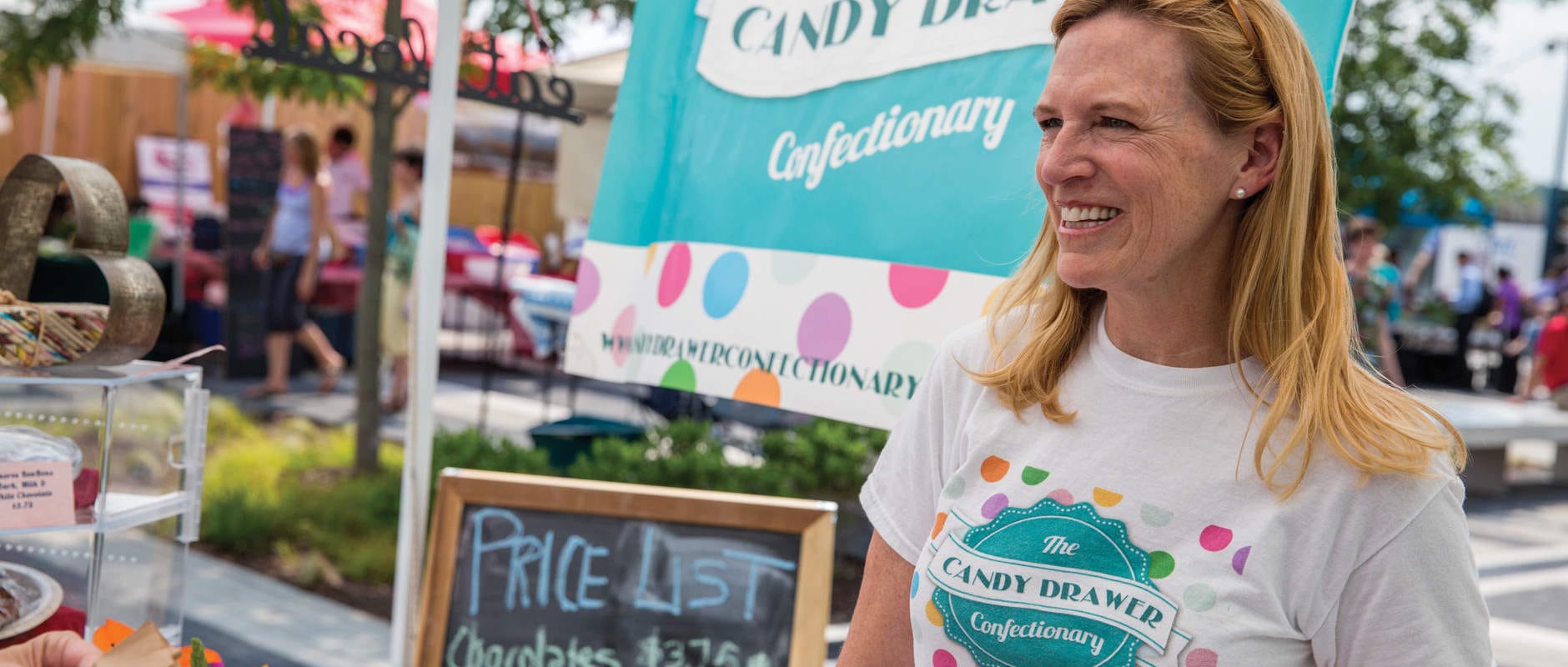 Woman wears promotional tshirt in front of similarly branded outdoor stall.