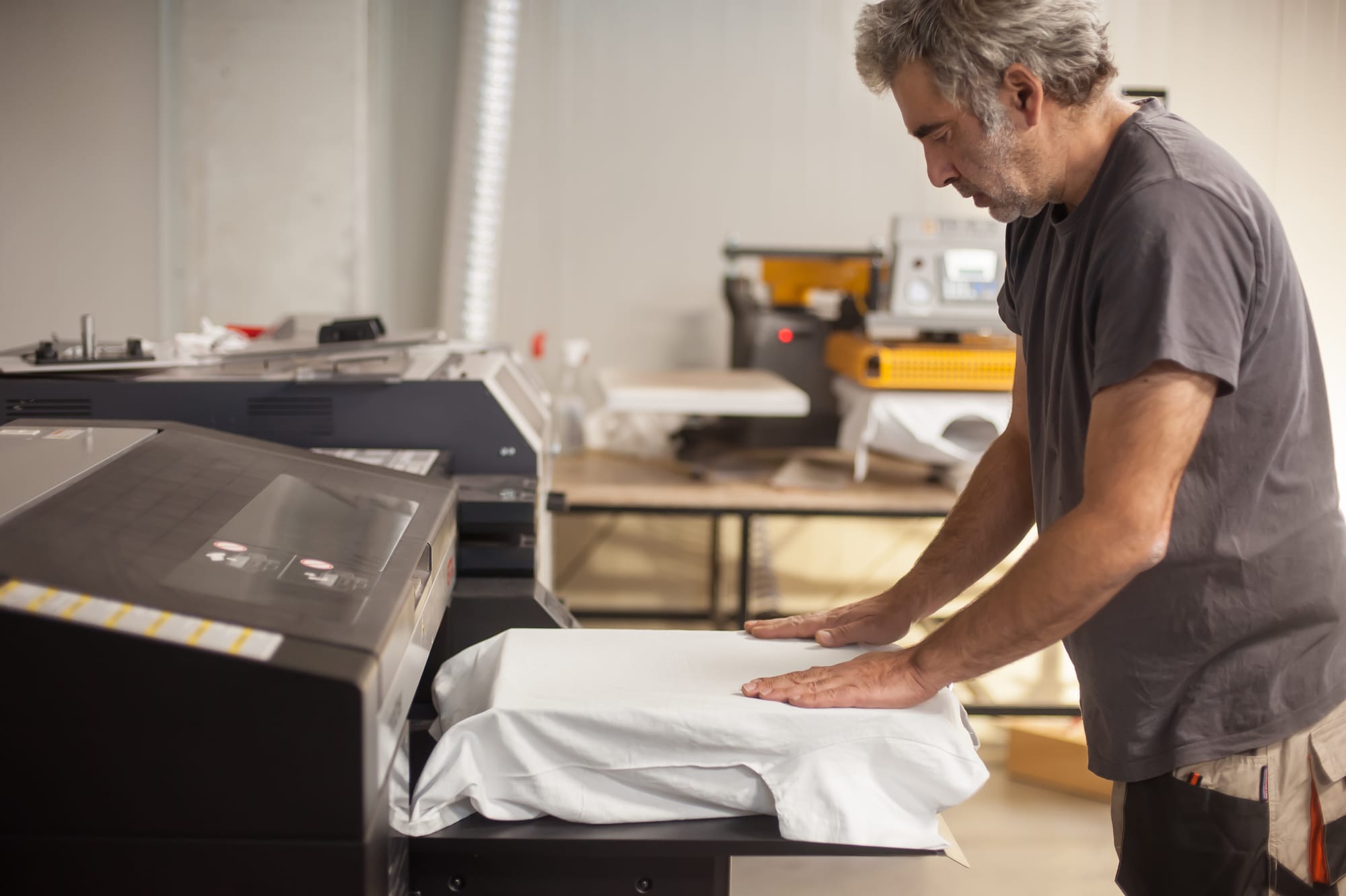 Professional graphic print technician placing fabric inside printer for direct-to-garment printing