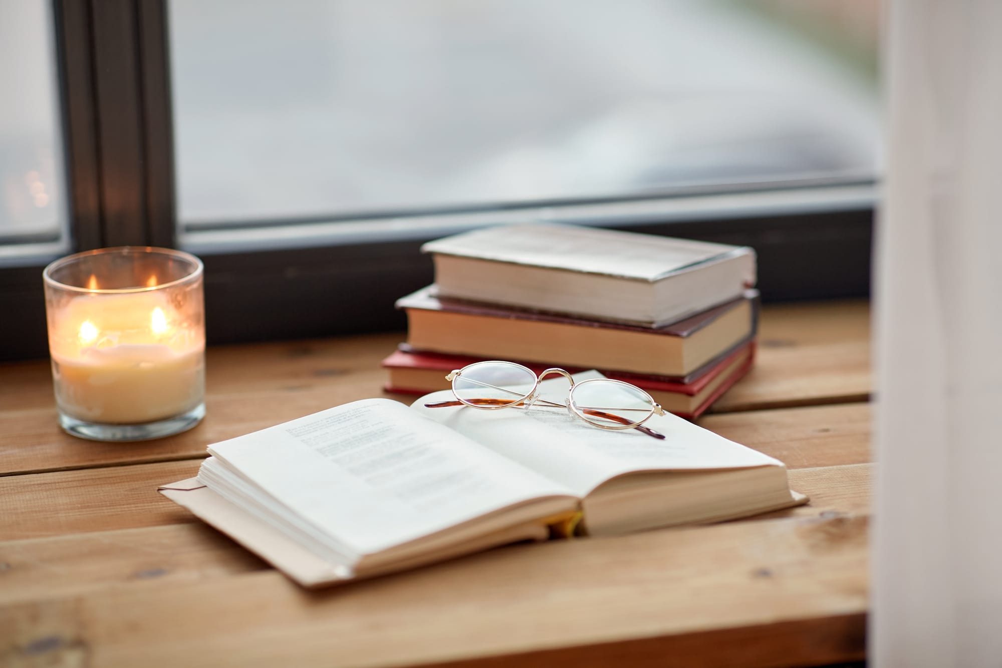 reading, leisure and objects concept - books, glasses and candle burning on window sill