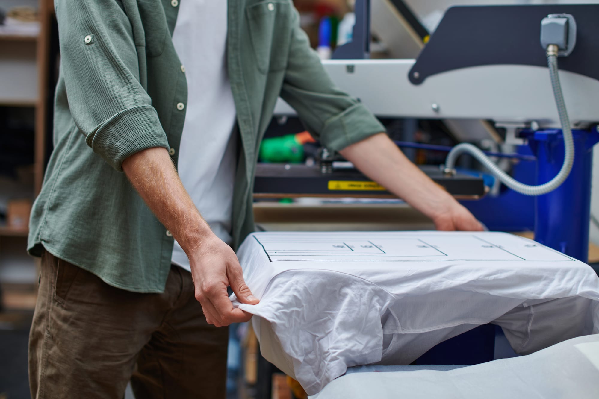 Printer holding a T-shirt with markings while working with screen printing machine in the print studio