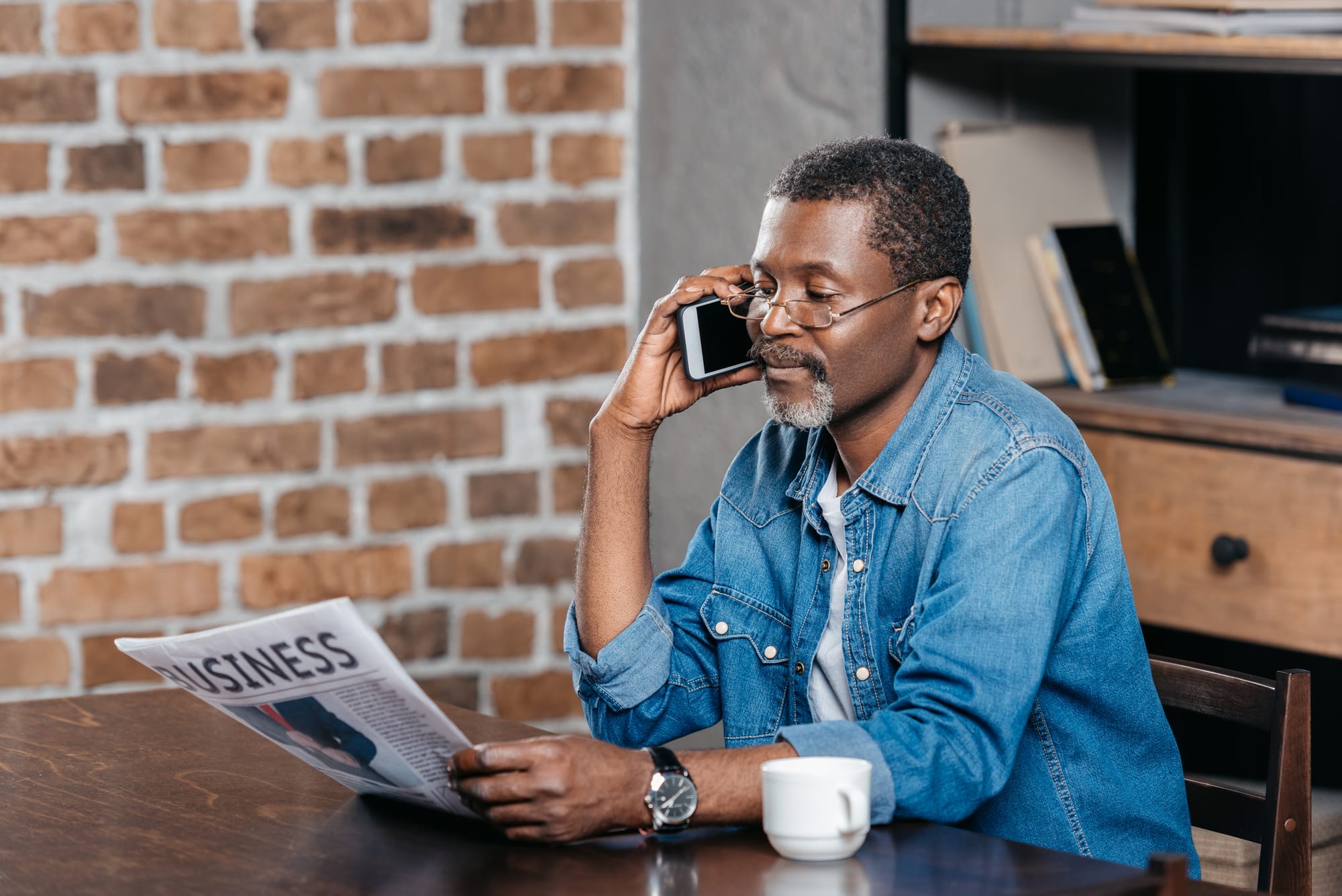 Man on phone reading newspaper.