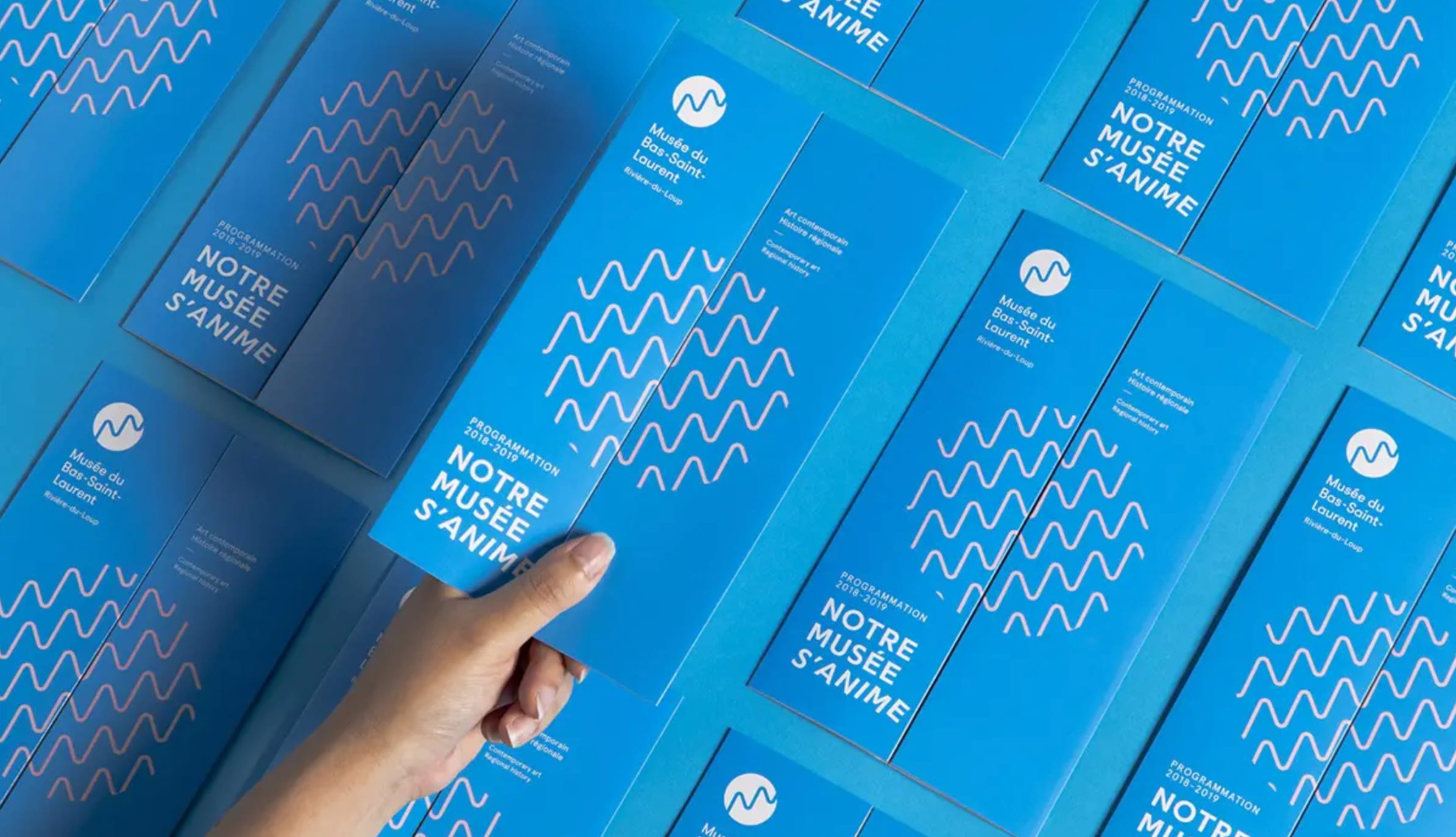 A hand picking up one of a number of Musée du Bas-Saint-Laurent brochures