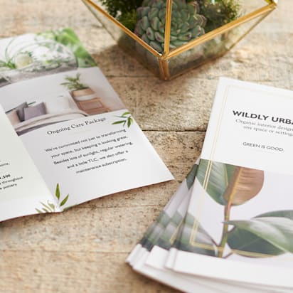 A business's trifold brochures are shown on a tabletop, one is opened with content to read and is beside a pile of folded ones.