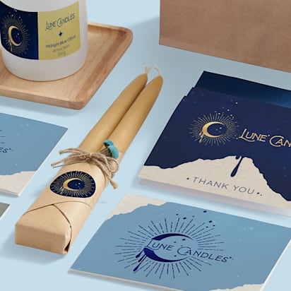 Close-up of print marketing materials for Luna Candles, including business cards, branded candles, stickers, and flyers.