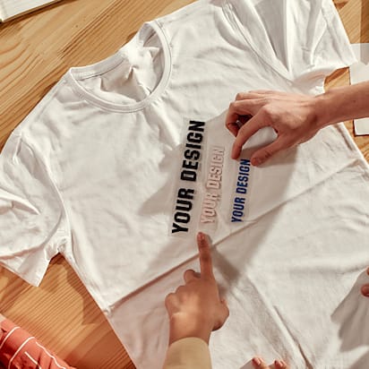 Top view of creative people trying on stickers with text, while discussing logo and design of T-shirt. Young man and women working together at custom T-shirt, clothing printing company. Cropped shot