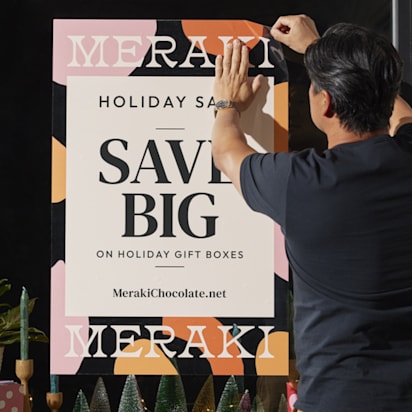 Small business owner applying a holiday sale decal to shop window – Christmas signage ideas in action.