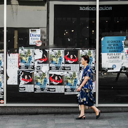 woman walking past window of posters