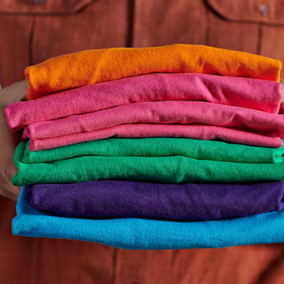 person carrying pile of multicolored t-shirts