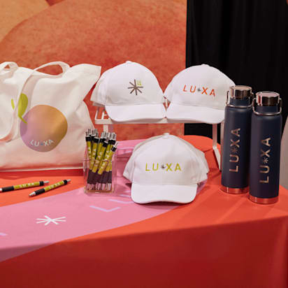 caps, tote bag and bottles all displaying branded print on colorful tradeshow desk