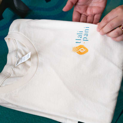 hands holding white branded t shirt for "tali pani" brand