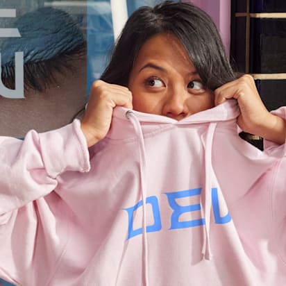 person peeks head above pink hoodie as they lift it over their head