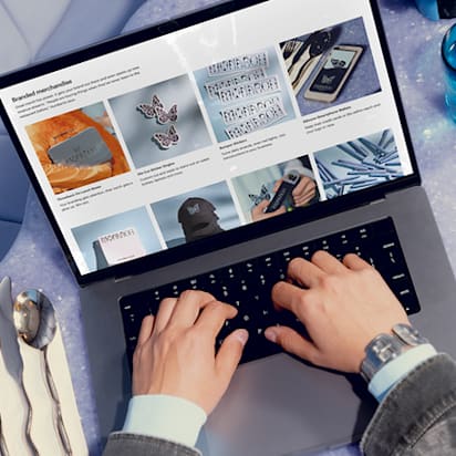 A person working on a laptop in a cozy environment, surrounded by everyday items like a cup of coffee and a notepad.