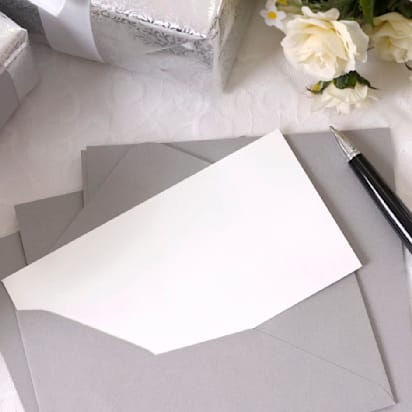 Writing paper or wedding invitation with envelope laid on bridal lace with several wedding gifts and white rose bouquets. Space for copy.