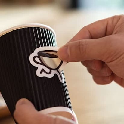 A small business owner putting a die-cut custom sticker on a coffee cup