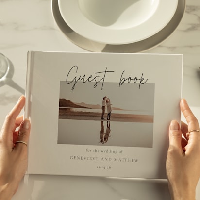 Close-up of a personalized wedding guest book held by a guest, featuring a photo of the couple and elegant script text.